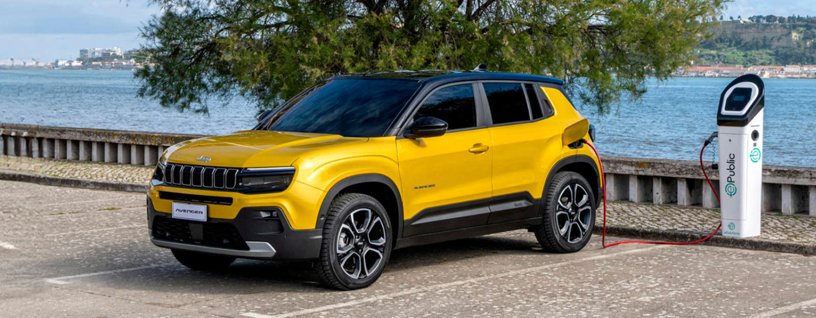 Jeep Avenger Electric жовтого кольору заряджається на стоянці біля моря